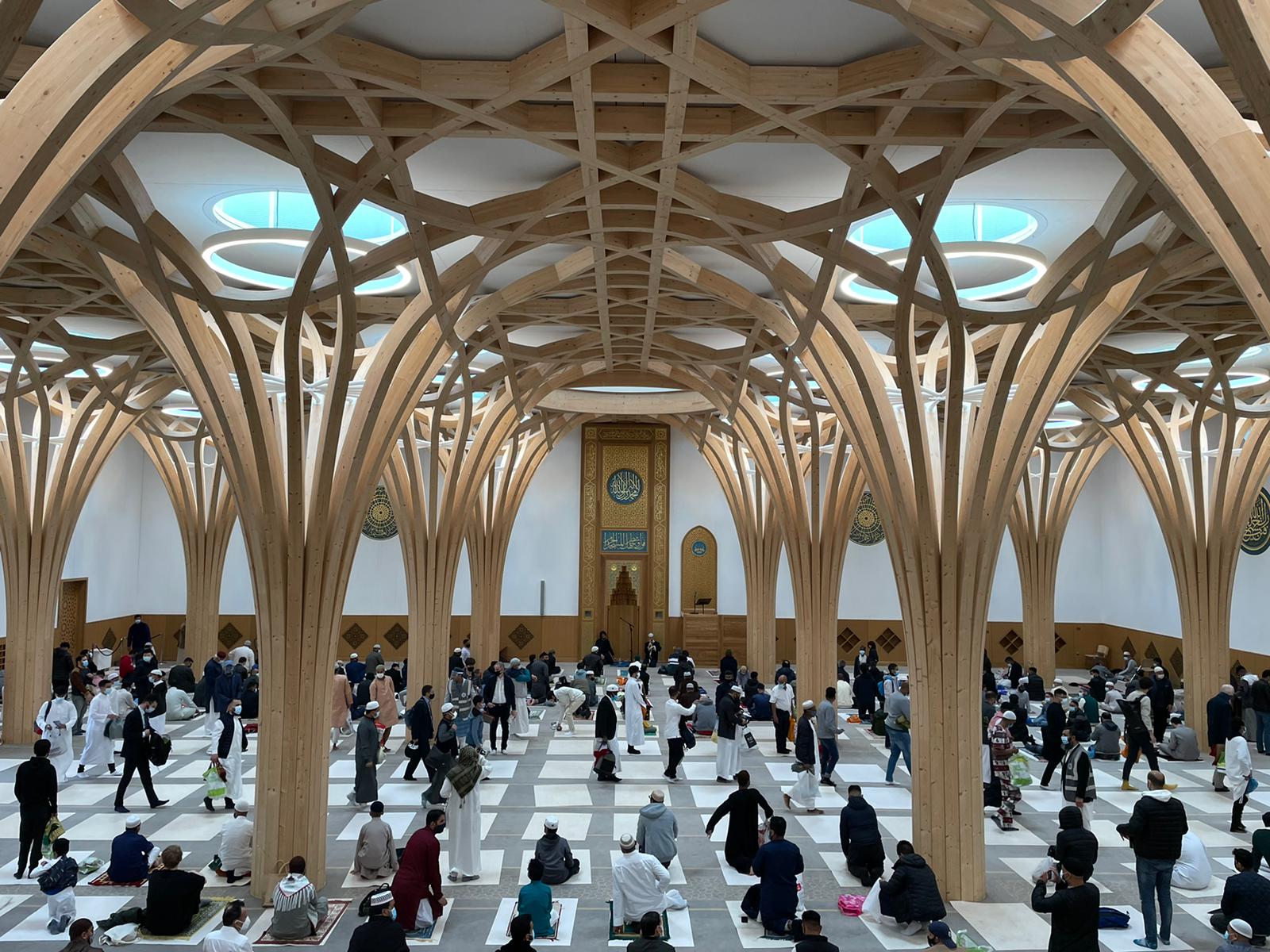 Extravagant timber pillars inside a mosque, with people praying