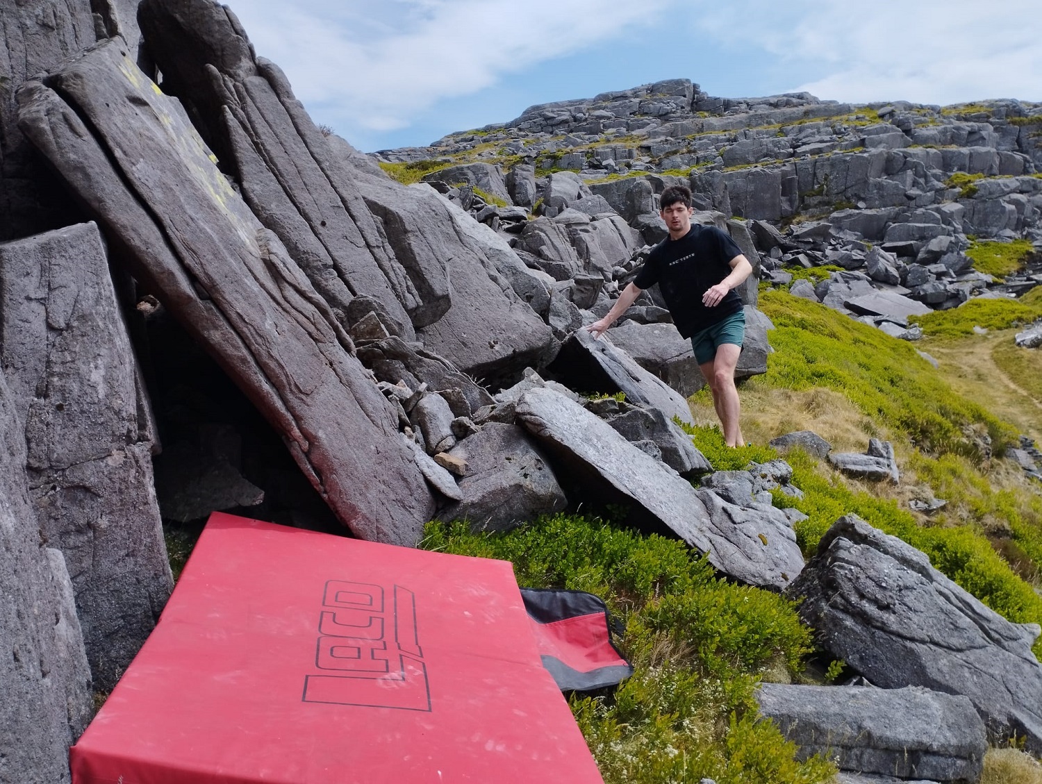 A person preparing to rock climb, with a red mattress at the foot of grey stone