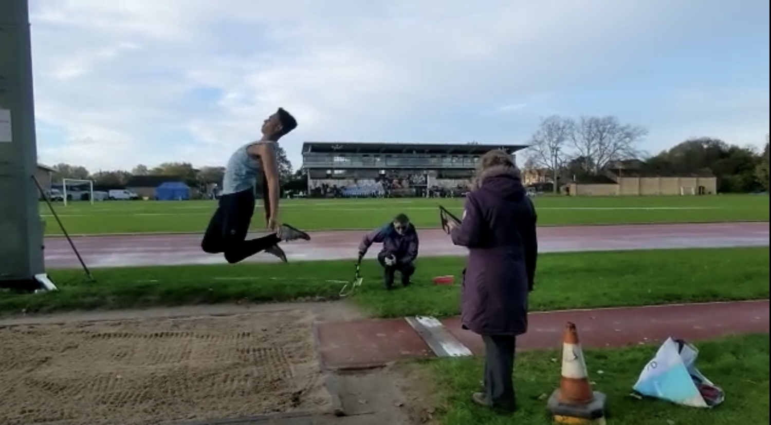 A man completing a long jump in the air over a sandpit
