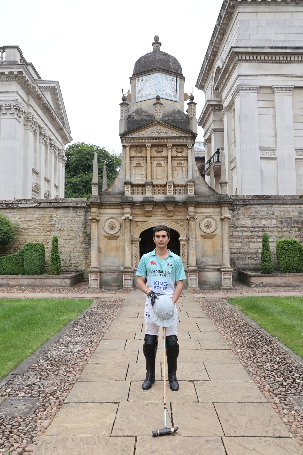 A man in polo kit standing in front of Caius College's Gate of Honour
