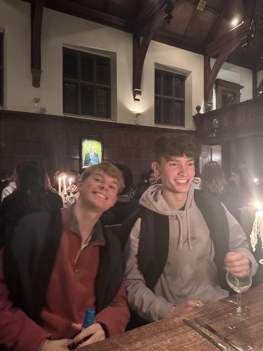 Two men in academic gowns and casual jumpers in Caius Hall