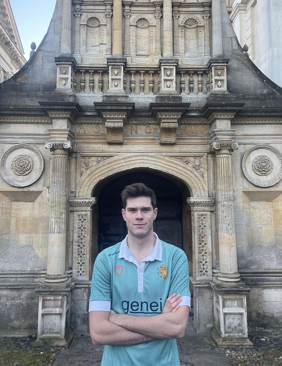 A man in a Cambridge hockey jersey in front of Caius' Gate of Honour