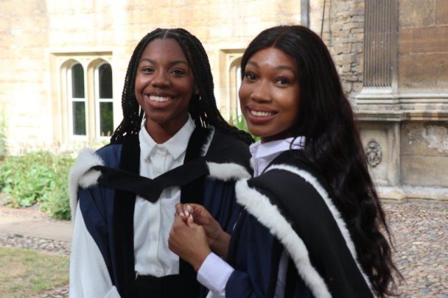 Two students in gowns smiling at the camera